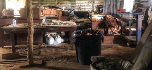 A cluttered, dimly lit room filled with old furniture, tools, and various items scattered around.