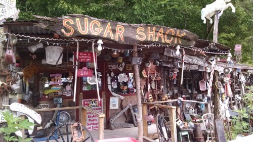 A rustic shop called "Sugar Shack" adorned with various vintage items and decorations, surrounded by greenery.