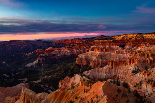 Vibrant sunset over layered red rock formations and valleys, with a colorful sky in the background.