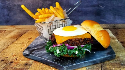 A gourmet burger with a fried egg, cheese, and fresh greens, served with a side of crispy French fries.
