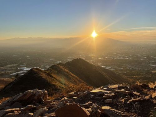 Sunrise over a mountainous landscape, casting golden light on the valley below, with rocky terrain in the foreground.
