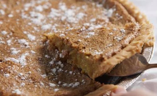 A close-up of a pie with a golden crust, dusted with powdered sugar, and a slice partially removed.