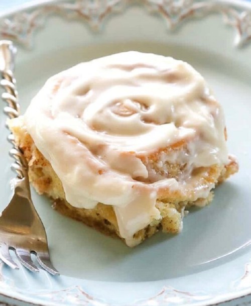 A frosted cinnamon roll on a decorative plate, with a fork beside it.