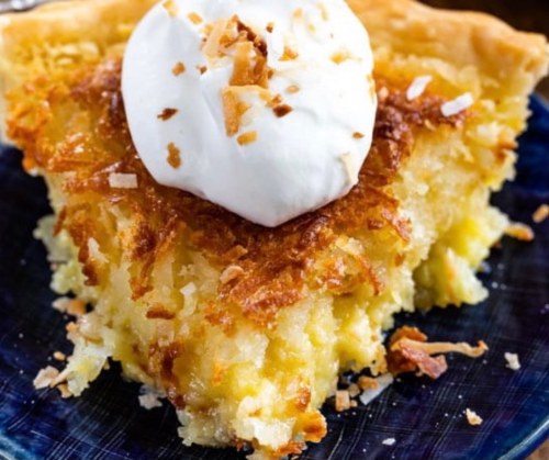 A slice of coconut pie topped with whipped cream and toasted coconut flakes on a blue plate.
