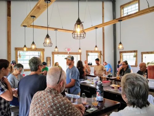 A busy bar scene with patrons chatting and enjoying drinks under warm pendant lights and wooden beams.