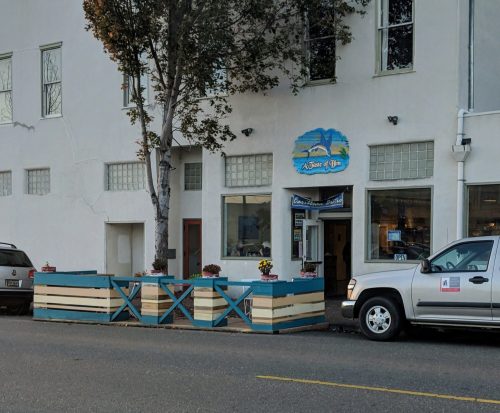 A storefront with a sign reading "A Place of Joy," featuring planters and a parked truck nearby.