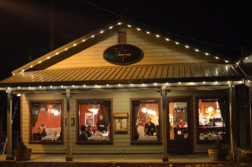 A cozy restaurant at night, warmly lit with string lights, featuring diners inside and a welcoming exterior.