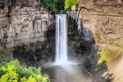A stunning waterfall cascading down rocky cliffs into a serene pool, surrounded by lush greenery.