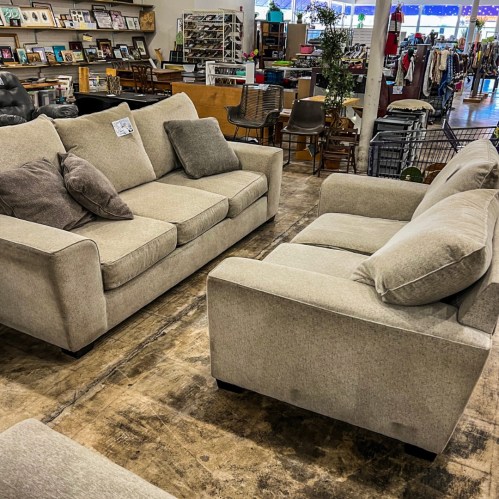 A light gray sofa set with cushions, displayed in a furniture store with various items in the background.