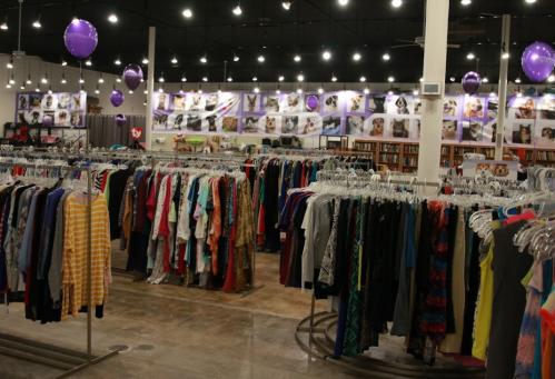A brightly lit thrift store with racks of clothing and a wall decorated with pet photos and purple balloons.