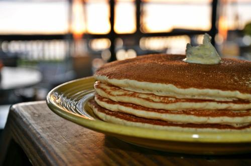 A stack of fluffy pancakes with a pat of butter on top, set against a sunset backdrop.