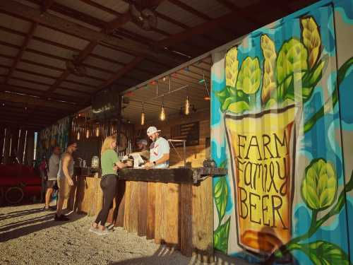 A vibrant outdoor bar with a colorful mural, where a customer interacts with a bartender. People enjoy the atmosphere.