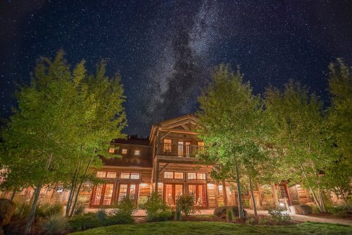 A cozy lodge surrounded by trees under a starry night sky, showcasing the Milky Way above.