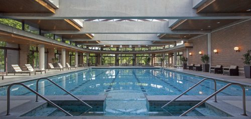 Indoor swimming pool with large windows, lounge chairs, and a modern architectural design.