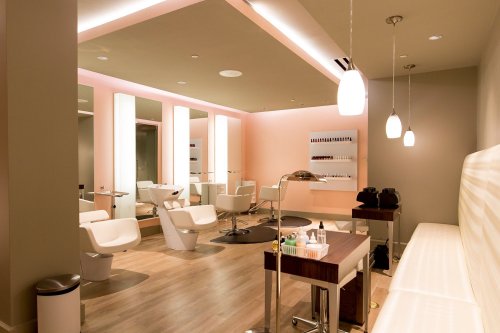 A modern salon interior featuring styling chairs, mirrors, and a nail station with soft lighting and a minimalist design.