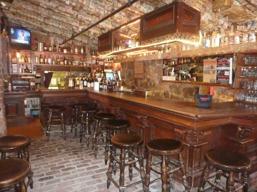 A cozy bar interior with wooden stools, a stone counter, and walls decorated with dollar bills.
