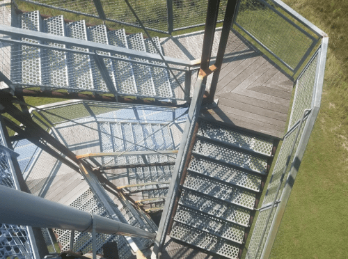 Aerial view of a spiral staircase with metal grating, leading down to a grassy area below.