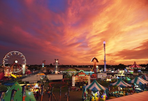 A vibrant sunset over a lively carnival, featuring rides, games, and colorful tents.