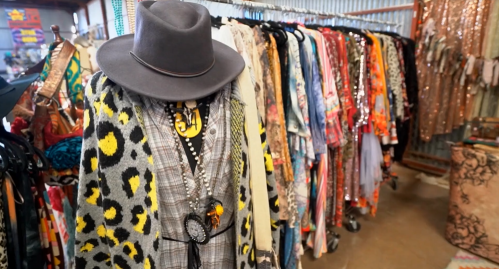 A colorful display of vintage clothing and accessories, including a hat and patterned garments on hangers.