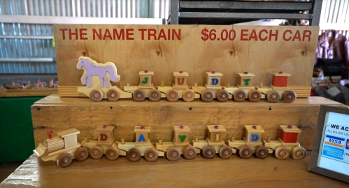 A wooden display of a name train with cars spelling "JUDY" and "DAVID," priced at $6 each.