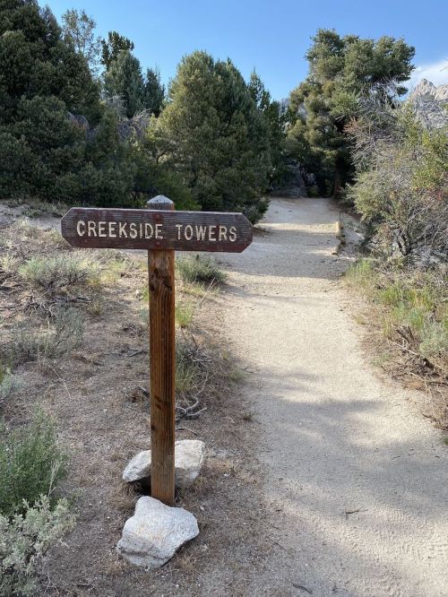 A wooden sign labeled "Creekside Towers" marks a dirt path surrounded by trees and shrubs.
