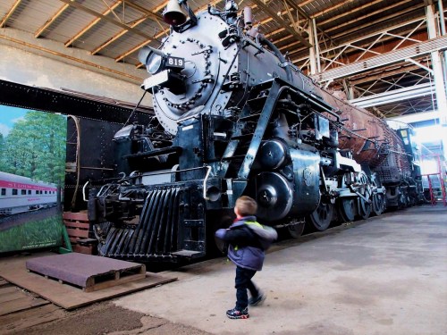 A child walks past a vintage steam locomotive inside a train museum.