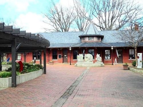 A brick building with a circular roof, surrounded by sculptures and trees, set in a landscaped outdoor area.