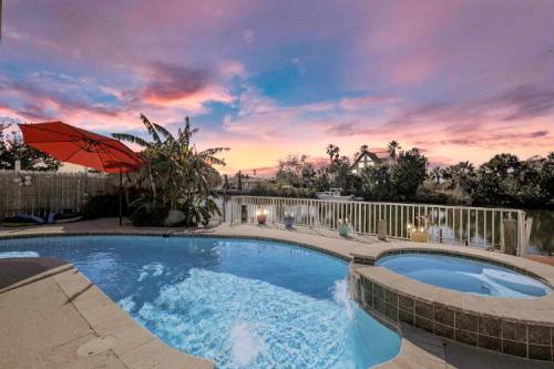 A serene poolside view at sunset, featuring a pool, hot tub, and vibrant sky with palm trees in the background.