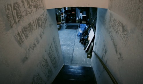 A dimly lit staircase leading down to a cluttered basement or garage space with various items and tools.
