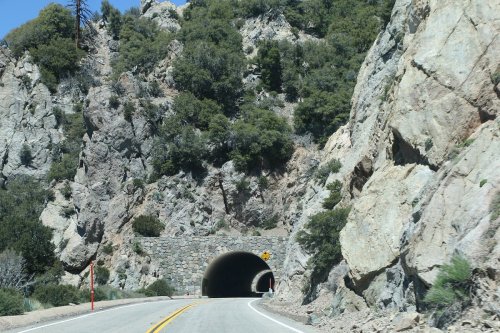 A winding road leads into a stone tunnel surrounded by rocky hills and greenery.