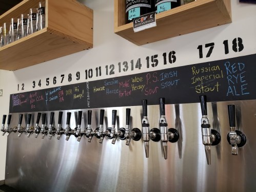 A row of beer taps with a chalkboard menu listing various brews above them, numbered 10 to 18.