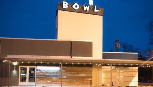 Exterior of a bowling alley named "BOWL" at dusk, featuring a modern design and illuminated signage.