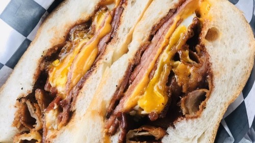 Close-up of a sandwich with layers of ham, cheese, and crispy fried onions on toasted bread.
