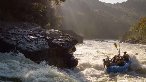 A group of people in a raft navigating a turbulent river surrounded by rocky cliffs and lush greenery.