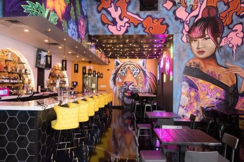 Vibrant restaurant interior featuring colorful murals, a tiger, and a stylish bar with yellow chairs.