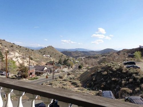 Scenic view of rolling hills and mountains under a clear blue sky, with a road and buildings in the foreground.