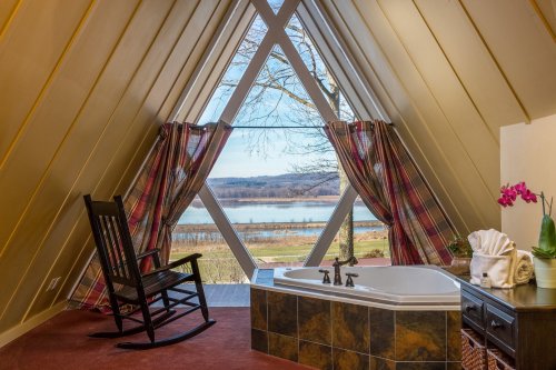 Cozy interior with a rocking chair and a spa tub, featuring large windows overlooking a scenic lake view.