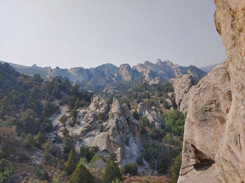 A rocky landscape with rugged cliffs and scattered trees under a hazy sky.