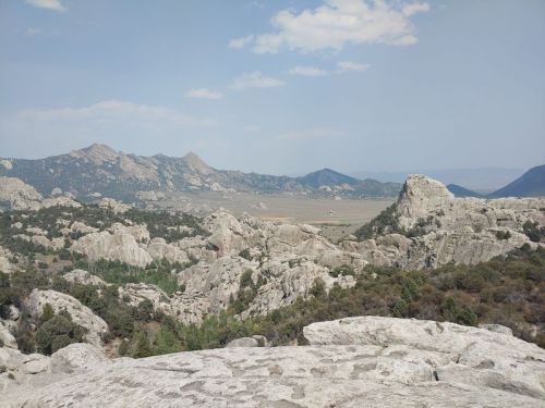 A panoramic view of rocky mountains and hills under a blue sky with scattered clouds.