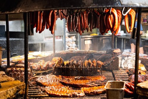 A smoky barbecue grill with various meats, including sausages and brisket, hanging and cooking over an open flame.