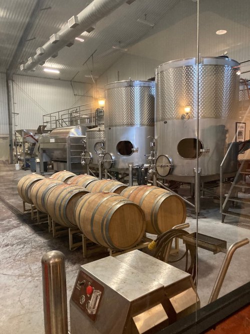 A winery interior featuring wooden barrels and stainless steel fermentation tanks.