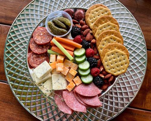 A colorful charcuterie board featuring meats, cheeses, crackers, fruits, and pickles arranged on a decorative plate.