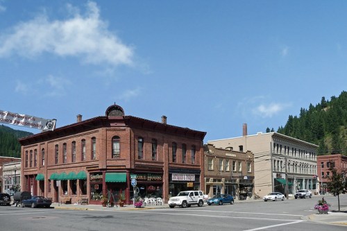 Historic buildings line a street in a small town, featuring brick architecture and green awnings under a blue sky.