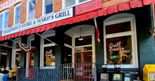 Exterior of Thompson's Store & Ward's Grill, featuring a red awning and open sign, with historic brick architecture.