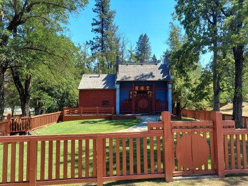 A colorful building with a red and blue exterior, surrounded by a wooden fence and trees under a clear blue sky.
