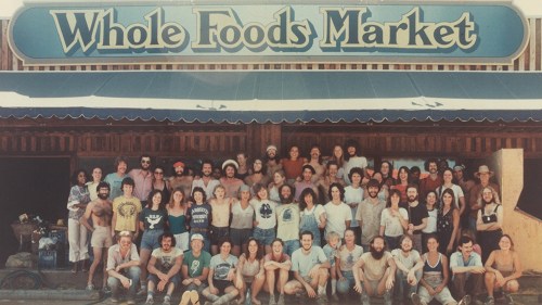 A large group of people poses in front of a Whole Foods Market sign, showcasing a diverse community and vintage style.