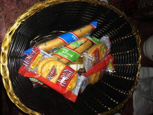 A black woven basket filled with various snacks, including crackers and cheese sticks.