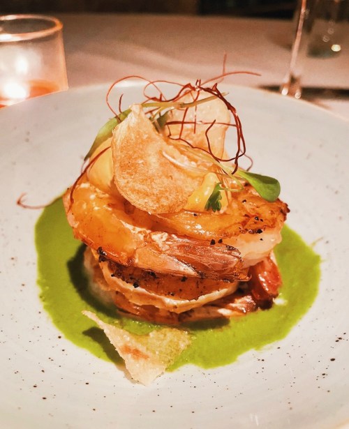 A gourmet dish featuring shrimp, crispy chips, and vibrant green sauce, elegantly presented on a light blue plate.