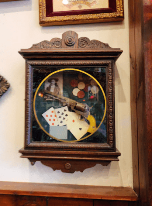 A vintage display case featuring a revolver, playing cards, and poker chips against a decorative background.