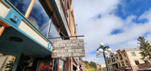 Sign for Historic Site: Saloon Number 10, where Wild Bill was shot on August 2, 1876, with a cloudy sky in the background.